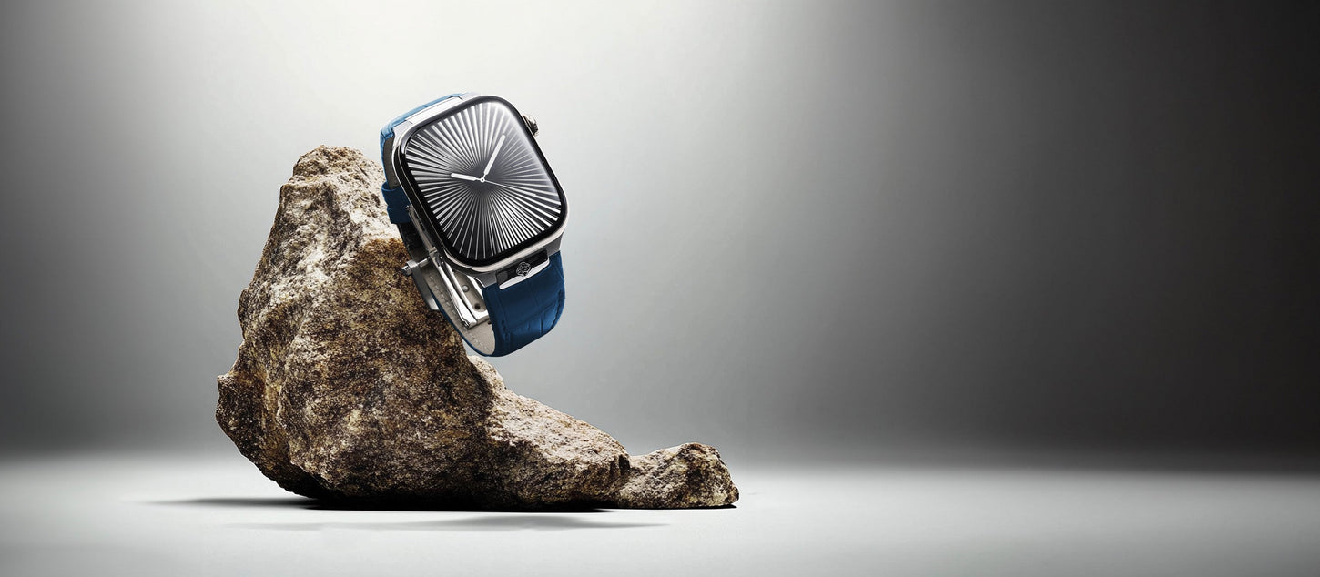 Square watch with sunburst dial and blue leather strap, displayed on rock.
